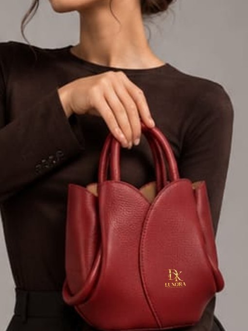A burgundy leather DK Luxora bag with petal-shaped panels, held by its top handles